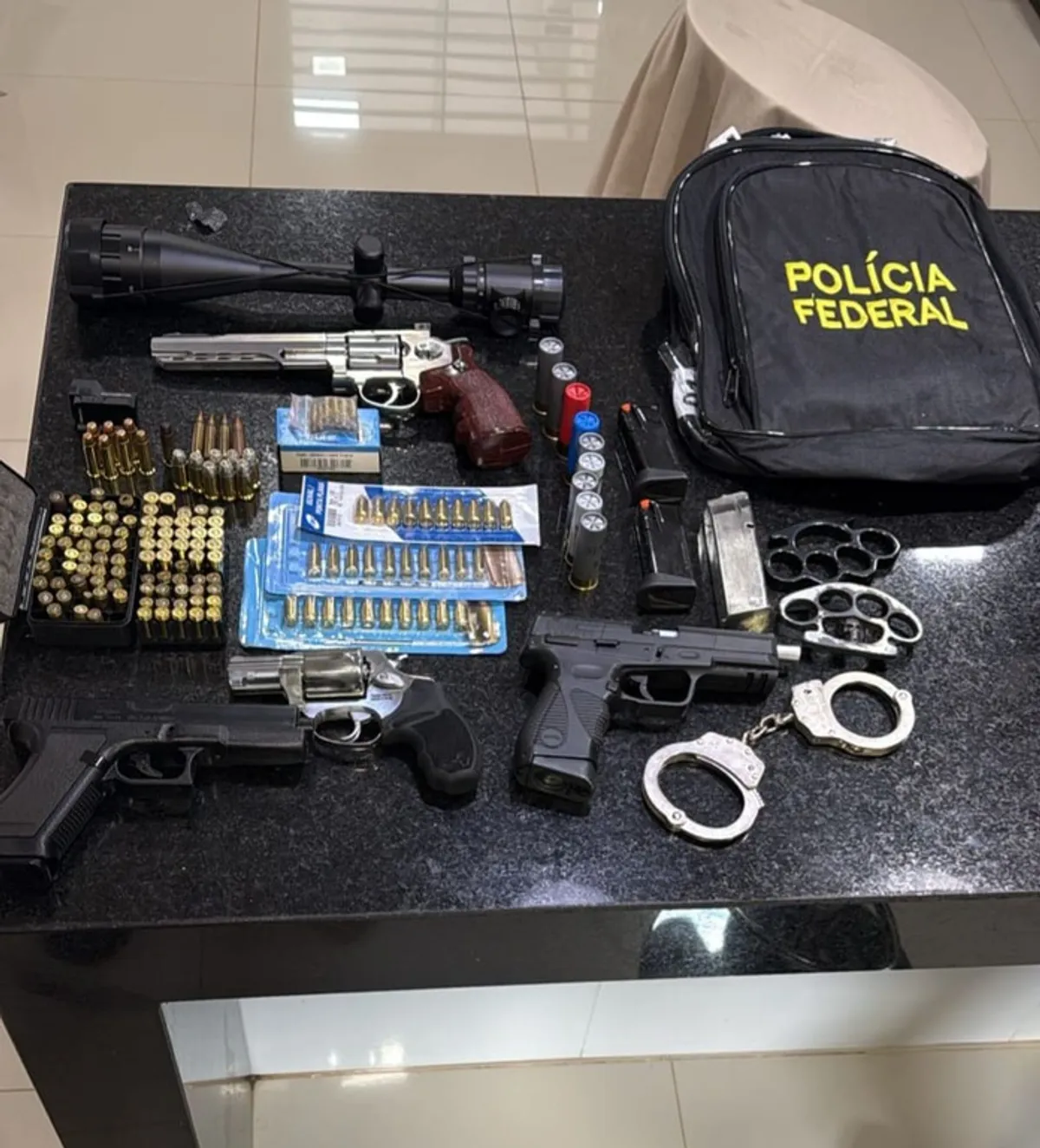 Agentes da Polícia Federal inspecionam armas e munições apreendidas durante a Operação Scutum 3 em Minas Gerais.